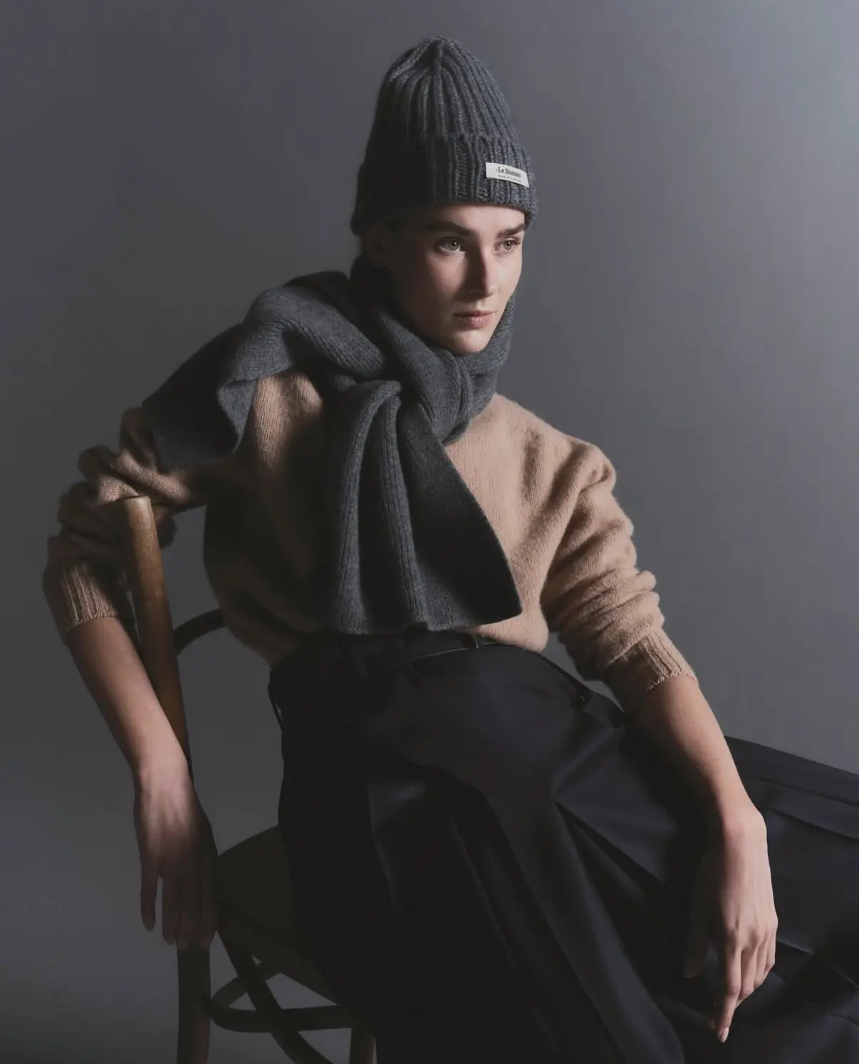 Femme assise portant un bonnet et une écharpe grise